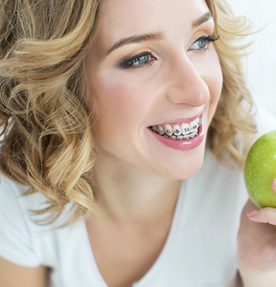 A young woman with braces holding a full apple in her hand
