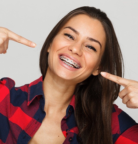 A young woman in a plaid shirt pointing to her traditional metal braces