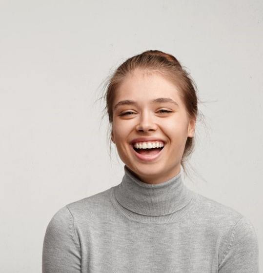 woman in gray sweater laughing after porcelain veneer placement