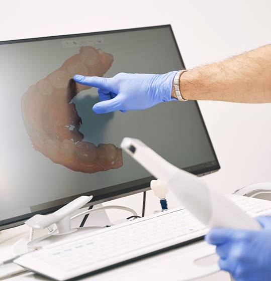 Gloved hand pointing to image of teeth on computer monitor