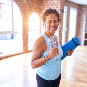 Smiling woman holding water bottle and yoga mat