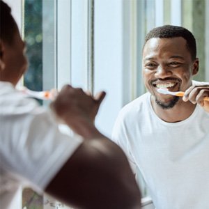 Man smiling at reflection while brushing his teeth